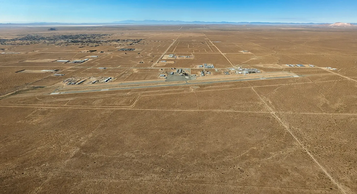 Aerial photograph of California City Municipal Airport: a single long runway across brown desert, with hangars and buildings beside it, a grid of dirt roads around it and the town in the distance.
